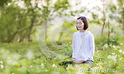 Asian woman is relaxingly practicing meditation yoga in forest full of daisy flower in summer to attain happiness from inner peace Stock Photo