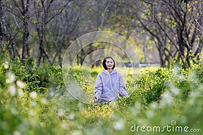 Asian woman is relaxingly practicing meditation yoga in the forest full of daisy flower in summer to attain happiness from inner Stock Photo