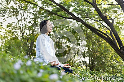 Asian woman is relaxingly practicing meditation yoga in forest full of wild flower in summer to attain happiness from inner peace Stock Photo