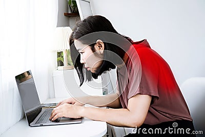 Asian woman's back and shoulder pain with incorrect posture while working on a computer and potential Kyphosis Stock Photo