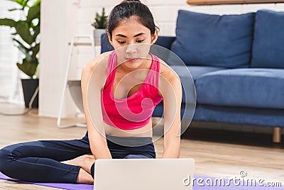 Asian woman searching video training onine on laptop and self training yoga pose in living room floor at home.Healthy lifestyle wi Stock Photo