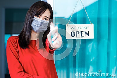 Asian woman shop owner smiling hanging label `Welcom we are open` and showing thump up Stock Photo