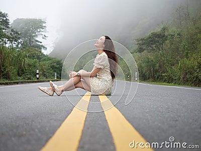 Asian woman sitting on road center line. road on mountain in foggy day. Stock Photo