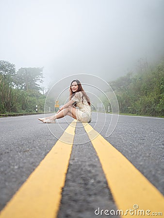 Asian woman sitting on road center line. road on mountain in foggy day. Stock Photo