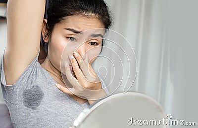 Asian woman smelling her smelly and sweating armpit and looking at a mirror Stock Photo