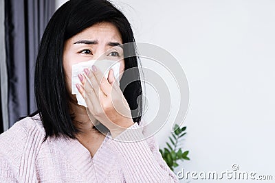 Asian woman sneezing, coughing allergic rhinitis to the bad weather hand holding paper tissue covering her runny nose Stock Photo