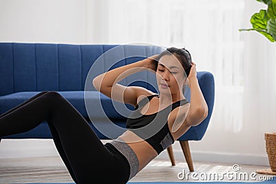 Asian woman in sportswear doing sit ups. Young woman making abdominal exercises at home Stock Photo