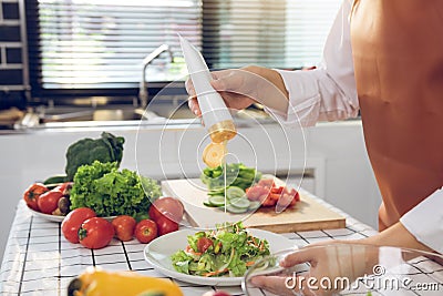 Asian woman squeezes mayonnaise on a salad plate at the kitchen cooking table Stock Photo