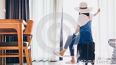 Asian women are staying in a hotel room with luggage.Open the curtain and door in the room looking to outside view.Travel in Stock Photo