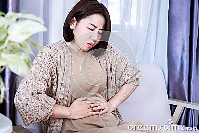 Asian woman suffering from stomachache and discomfort due to food poisoning Stock Photo