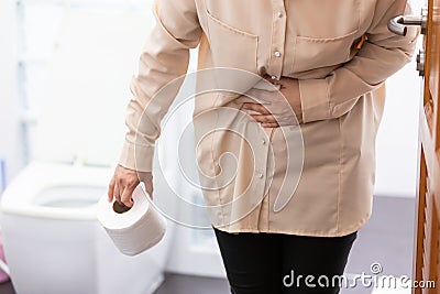 Asian woman suffers from diarrhea holding tissue roll or toilet paper near a toilet bowl,girl have abdominal pain,stomachache, Stock Photo