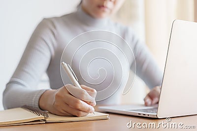 Asian woman is taking notes and using laptop computer at office Stock Photo