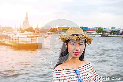 Asian woman tourist wear hat standing smiling with the background is a view of chao phraya river and pagoda arun temple landmark Stock Photo