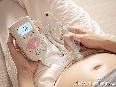 Asian woman using pocket fetal doppler to monitor baby heart beat. expectant mother happy and smile when examine belly. Stock Photo