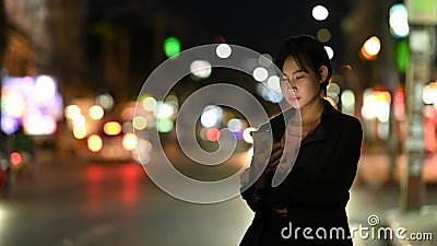 Asian woman waits for her private taxi by using a transportation app on the night street Stock Photo