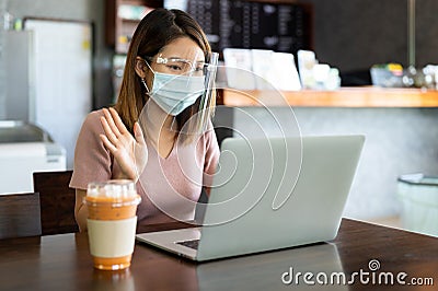 Asian woman wearing face shield and protective mask working on laptop in coffee shop Stock Photo