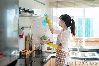 Asian woman wearing rubber protective gloves cleaning kitchen cupboards in her home during Staying at home using free time about Stock Photo