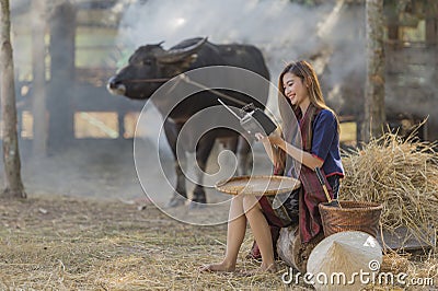 Asian woman wearing traditional thai culture,in field,vintage style listening radio on buffalo and farm background Stock Photo