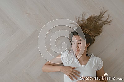 Asian woman wears white t-shirt lie on the wooden floor exhaustedly. Stock Photo