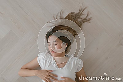 Asian woman wears white t-shirt lie on the wooden floor exhaustedly. Stock Photo