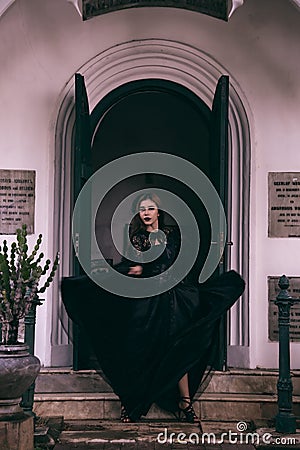 an Asian woman with a witch-like appearance flung her all-black skirt in the air as she stood in front of a cemetery Stock Photo