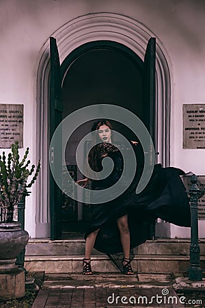 an Asian woman with a witch-like appearance flung her all-black skirt in the air as she stood in front of a cemetery Stock Photo