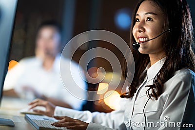 Asian woman work as customer support service or call center phone operator, using computer, microphone headset, late night shift Stock Photo