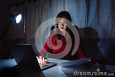 Asian woman working late at night reading document with laptop computer home office workhard Stock Photo