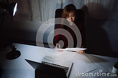 Asian woman working late at night reading document with laptop computer home office workhard Stock Photo