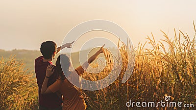 Asian woman and man standing and point hand in meadow and looking far away at sunrise time Stock Photo