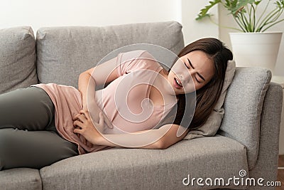 Asian women with menstrual pain at abdomen And the face expression. Asia woman having painful while lying on the sofa at her home Stock Photo