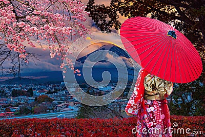 Asian women wear Japanese kimonos. Holding a red umbrella at Mount Fuji and cherry blossoms in Japan Stock Photo