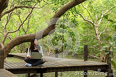 Asian women working and drinking coffee after education nature and forest input the laptop under big tree. The mangrove forest n Stock Photo