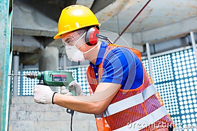 Asian worker drilling in construction site wall Stock Photo