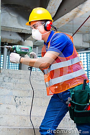 Asian worker drilling in construction site wall Stock Photo