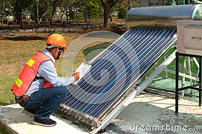 The Asian worker in uniform and helmet checks concentrating Solar Power with Flat Plat collector and Evacuum Tube Collector. Stock Photo