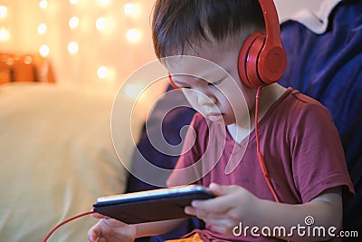 Asian 2 -3 years old toddler boy child listening to music with headphones from smartphone, Kids playing with phone in bedroom at h Stock Photo