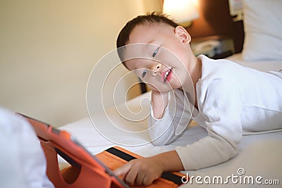 Asian 2-3 years old toddler boy child sitting in bed watching a video from tablet pc Stock Photo