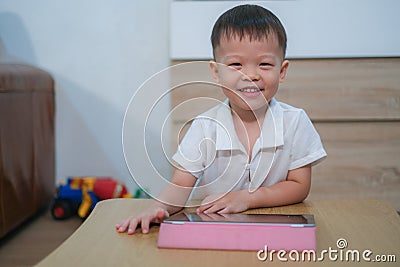 Asian 2 - 3 years old toddler boy child smiling and looking at camera while using tablet pc computer, Learning Tablet for Kids Stock Photo