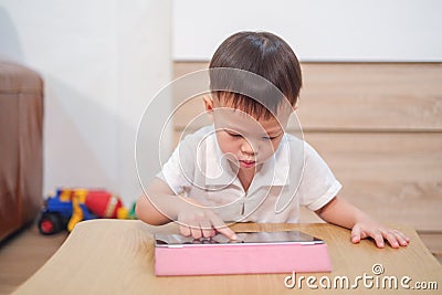 Asian 2 - 3 years old toddler boy using tablet pc playing game, watching a video from tablet pc. Gadget-addicted kid Stock Photo