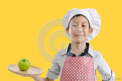 Asian young chef present green apple on wooden tray, yellow back Stock Photo