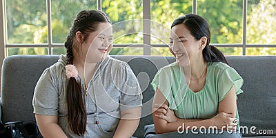 Asian young chubby down syndrome autistic autism little cute daughter sitting on cozy sofa smiling laughing having good time and Stock Photo