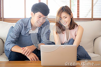 Asian young couple using laptop computer think and searching internet together, man and woman casual smiling work at home Stock Photo