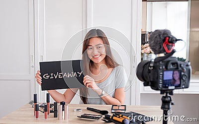 Asian young female blogger giveaway gift to fan following channel while recording vlog video with makeup cosmetic at home online Stock Photo