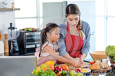 Asian young female chef mother wears apron teaching little cute girl daughter cooking preparing making delicious sandwiches with Stock Photo