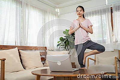 Asian young girl doing Yoga, follow online trainer in laptop at home. Active Beautiful sportswoman doing lockdown activity in Stock Photo