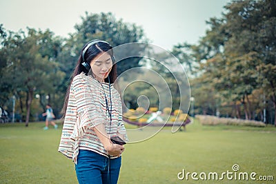 Asian young girl stands listening to music from a smartphone using headphones and copy space. At public park the city center happy Stock Photo