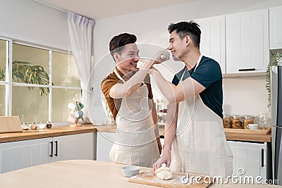 Asian young LGBTQ male gay family enjoy bake bakery in kitchen at home. Attractive handsome romantic man couple wear apron feeling Stock Photo
