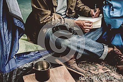 Asian young man sitting is holding a pen writing note of letter memorize memories on book in outside the tent. Loneliness Stock Photo