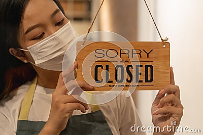 Asian young owner retail,coffee shop woman turning sign board to closed with wearing face mask,protection to pandemic of Stock Photo